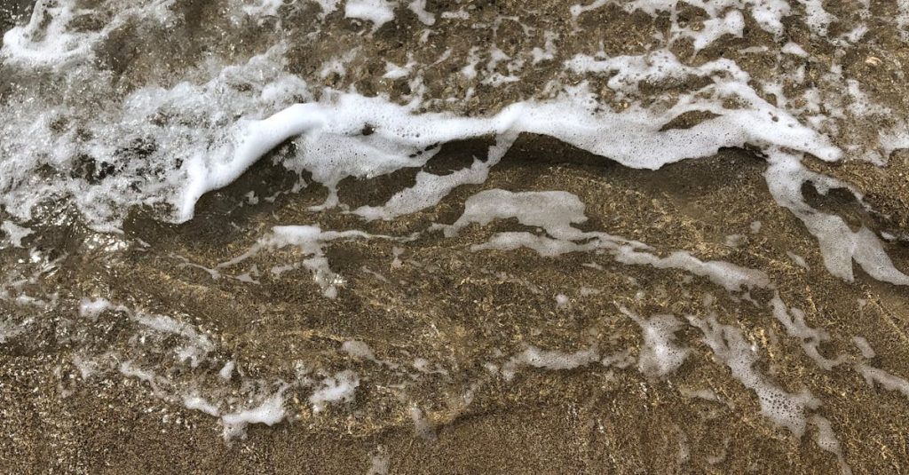 Close-up of ocean waves crashing onto a sandy beach, creating foam and texture.