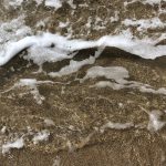 Close-up of ocean waves crashing onto a sandy beach, creating foam and texture.