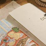 Top view of a sketchbook, plants, and tea on a wooden desk.